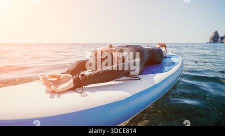 Paddleboard Yoga Ocean Man pratique le yoga pose sur Paddleboard à Ocean at Sunset Banque D'Images