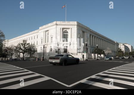 Vue d'une voiture grise moderne traversant le trottoir noir et blanc devant un énorme bâtiment gouvernemental blanc, Washington D.C. Banque D'Images