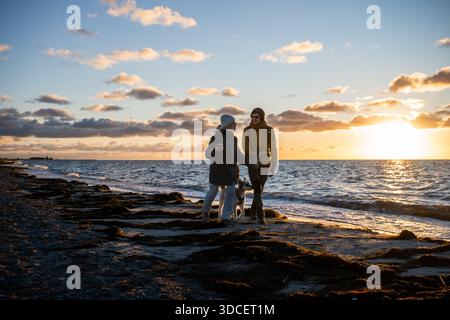 Couple marchant avec un chien le long de la plage de la mer Baltique au coucher du soleil Banque D'Images