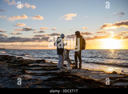 Couple marchant avec un chien le long de la plage de la mer Baltique au coucher du soleil Banque D'Images