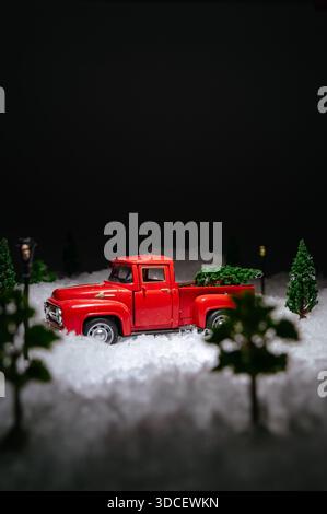 Une voiture jouet rouge transporte un arbre de Noël le long d'une route enneigée Banque D'Images
