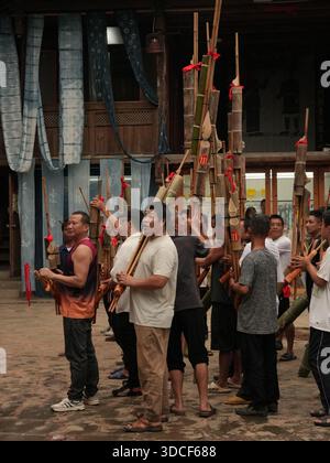 Qiandongnan, Chine - 30 septembre 2025 : vue d'un groupe d'hommes jouant d'instruments traditionnels devant un bâtiment en bois, leur musique remplissant le Banque D'Images