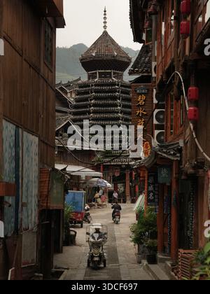 Qiandongnan, Chine - 30 septembre 2025 : vue d'une imposante pagode traditionnelle en bois s'élevant au-dessus de la rue animée, encadrée par des buil en bois altérés Banque D'Images