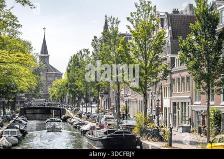 Amsterdam, pays-Bas - 29 juillet 2019 : vue sur un canal reflétant le ciel, des bateaux glissant sous des ponts et des bâtiments bordant la voie navigable, avec lu Banque D'Images