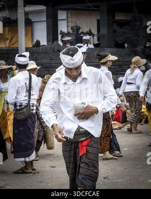 Canggu, Indonésie - 19 mars 2023 : vue d'un homme en tenue traditionnelle marchant avec but au milieu d'une foule près d'un temple balinais. Banque D'Images