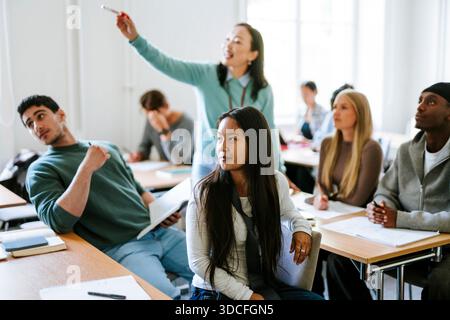 Jeune femme aux cheveux longs écoutant le professeur tout en étant assise au bureau dans la salle de classe au collège Banque D'Images
