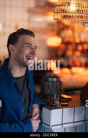 Homme heureux appuyé sur le comptoir du bar tout en dégustant un cocktail au bar Banque D'Images