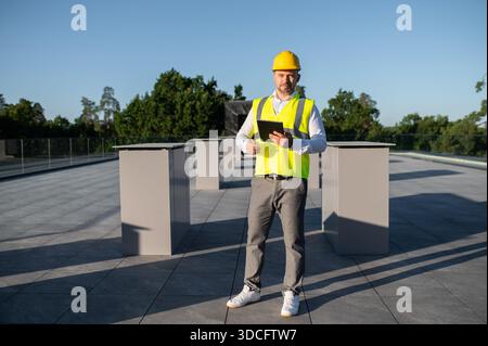 Travailleur inspectant les panneaux solaires sur le toit tenant la tablette numérique dans les mains Banque D'Images