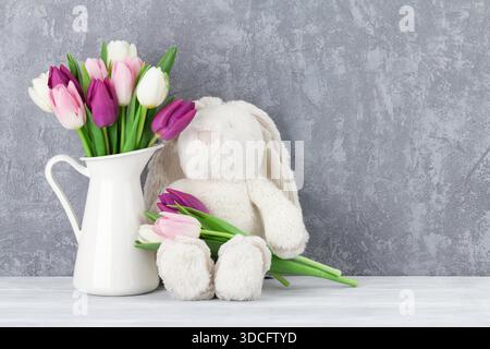 Bouquet de tulipes colorées et lapin jouet en avant du mur de pierre. Carte de Pâques. Avec l'espace pour vos messages d'accueil Banque D'Images