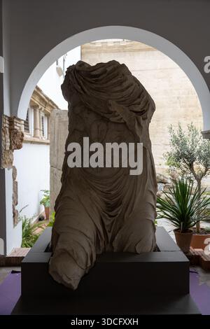 Cordoue, Espagne - 21 mai 23 : une statue ancienne partiellement préservée drapée de tissu, exposée dans un cadre architectural avec des plantes en arrière-plan Banque D'Images