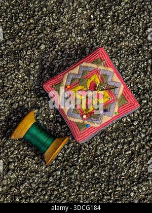 Image minimale de nature morte d'un coussin d'épingle coloré fait à la main avec des épingles et une bobine de coton en bois avec du coton vert sur un fond de tarmac noir Banque D'Images