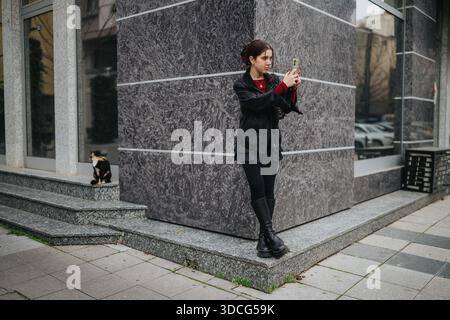 Femme prenant un selfie avec smartphone dans la rue de la ville à côté d'un chat sur les marches Banque D'Images