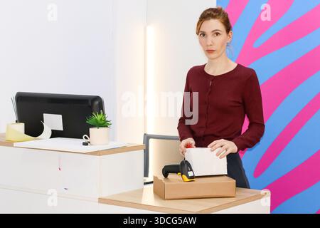 Employé en chandail Bordeaux tenant le colis et le lecteur de code-barres sur carton dans la zone de ramassage. Banque D'Images