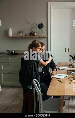 Fille embrassant père travaillant sur ordinateur portable à la maison Banque D'Images