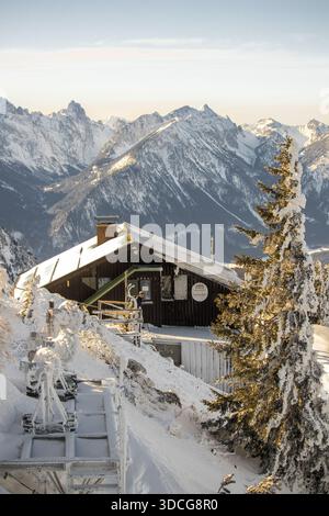 Vue d'une cabane enneigée nichée au milieu des sommets givrés, avec un pin couvert de neige debout de garde dans la lumière du soleil croustillante et dorée, Bavière, Banque D'Images