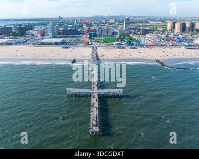 Vue aérienne d'un quai qui s'étend dans l'océan, contrastant avec le paysage urbain, y compris l'emblématique Wonder Wheel et l'amuse vibrante de Coney Island Banque D'Images