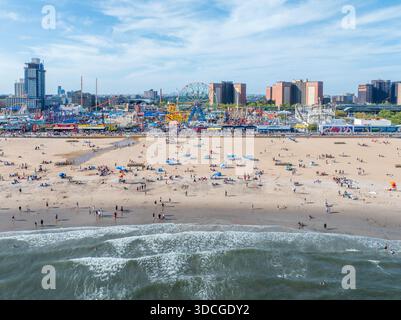 Vue aérienne des bains de soleil tachetant la plage dorée, les célèbres montagnes russes Wonder Wheel et Cyclone se dressent contre les gratte-ciel de Brooklyn Banque D'Images