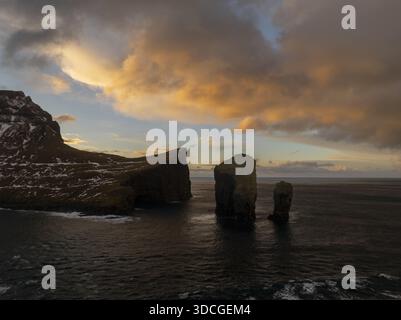 Vue aérienne de la pile de la mer de Drangarnir perçant à travers les eaux sombres sous un ciel enflammé avec les teintes flamboyantes de coucher de soleil, Vagar, Vagar, îles Féroé Banque D'Images