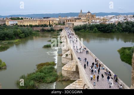 Cordoue, Espagne - 21 mai 23 : vue aérienne d'un pont de pierre historique sur une rivière, avec des gens marchant dessus, entouré de verdure et de bâtiments de la ville Banque D'Images