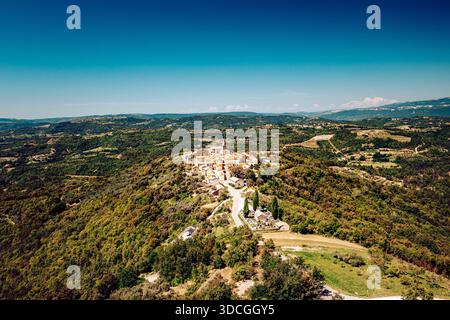 Vue aérienne du village ensoleillé et couvert de terre cuite de Draguć niché parmi les collines verdoyantes, une tapisserie de lumière et d'ombre sous un ciel clair, Banque D'Images