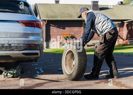 L'achèvement et l'autonomie capturés comme un homme senior roule un pneu de voiture enlevé, terminant le changement de pneu avec confiance et fierté de faire Banque D'Images