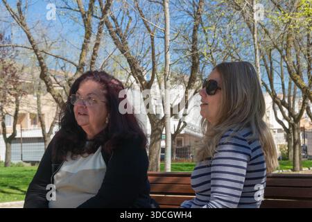 Deux femmes assises sur un banc dans un parc profitent d'une conversation par une journée ensoleillée Banque D'Images