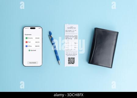 Smartphone affichant le tableau de bord de vue d'ensemble des dépenses à côté du reçu papier sur fond bleu, illustrant l'application de finance moderne, le logiciel de comptabilité, le bus Banque D'Images