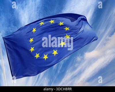 Drapeau de l'UE flottant flotter nuages tourbillonnants élevés ciel occupé ensoleillé intelligent audacieux UE Europe européenne Communauté drapeau volant flotter action gel dans la brise rétro-éclairé contre les nuages et le ciel bleu dramatiques ouverts. étoiles jaunes / dorées en vedette Banque D'Images