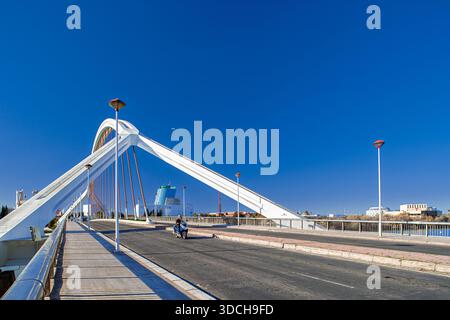 Un scooter traverse le pont Barqueta de Séville par temps clair. Merveille architecturale, construite à l'origine pour Expo 92. Photographie de voyage lumineuse et ensoleillée. Banque D'Images