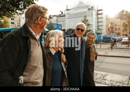 Groupe d'amis seniors marchant côte à côte sur le trottoir en ville Banque D'Images