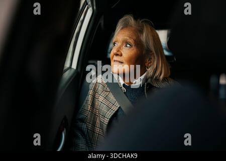 Femme âgée regardant par la fenêtre tout en étant assise dans la voiture Banque D'Images