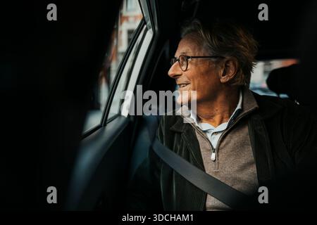 Heureux homme senior regardant par la fenêtre tout en voyageant en voiture Banque D'Images