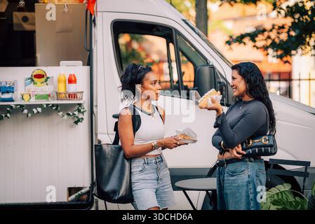 Amies féminines multiraciales parlant les unes avec les autres tout en mangeant des apéritifs près du camion de nourriture Banque D'Images