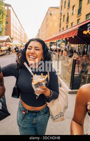 Heureuse jeune femme tenant des frites marchant avec des amis dans la rue Banque D'Images