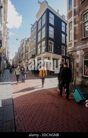 Femme à la mode se promène dans une rue animée à Amsterdam entourée de touristes portant des valises, tenant des parapluies, faisant du vélo dans la rue pleine de bars. Banque D'Images