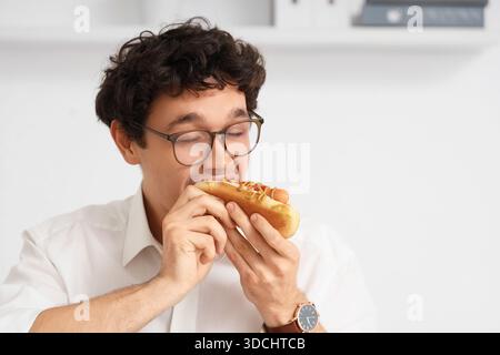 Jeune homme d'affaires mangeant un hot dog savoureux au bureau, gros plan Banque D'Images