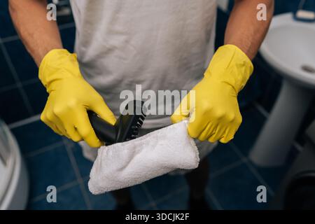 Cliché recadré des mains masculines de femme de ménage, protégées par des gants en caoutchouc jaunes, attachant la housse en tissu microfibre blanc à la buse du nettoyeur vapeur, préparation Banque D'Images