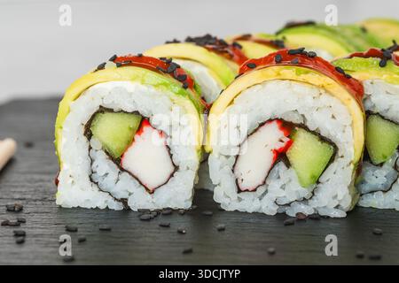 Rouleaux de sushi avec imitation crabe et concombre, nappés de tranches d'avocat et arrosés de sauce rouge épicée. Banque D'Images