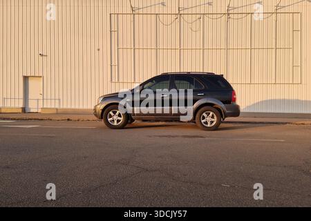 SUV noir sur la rue dans le quartier industriel au coucher du soleil. Vue de profil latérale grand angle de KIA Sorento garé dans une ville près d'un mur rayé blanc. Banque D'Images