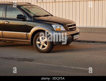 L'avant du SUV noir jette un coup d'œil à partir du bord du cadre. Coin avant gauche de KIA Sorento sombre garé sur une rue le long d'un mur blanc au coucher du soleil. Banque D'Images