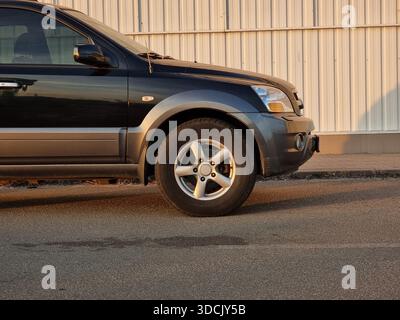 L'avant du SUV noir jette un coup d'œil à partir du bord du cadre. Vue latérale de la partie avant de la voiture sombre garée sur une rue le long du mur blanc au coucher du soleil. Banque D'Images