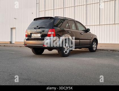 Noir KIA Sorento garé dans une rue. Vue arrière de trois quarts de SUV sombre dans le quartier industriel dans les faisceaux de soleil couchant. Banque D'Images