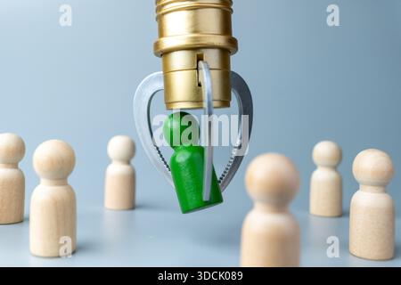 Une figure en bois vert étant choisie par une griffe mécanique parmi d'autres figures. Embauche, ressources humaines, leadership, recrutement et sélection des talents Banque D'Images