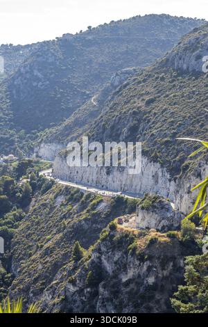 Vue sur une route sinueuse creusée dans le flanc accidenté et ensoleillé de la montagne, avec une végétation luxuriante accrochée aux pentes d'Èze, Provence-Alpes-Côte d'Azur Banque D'Images
