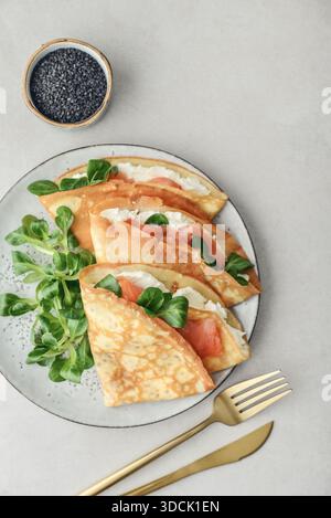 Crêpes ou crêpes fines avec saumon légèrement salé, fromage à pâte molle et salade de maïs ou laitue d'agneau sur une assiette vue de dessus de gros plan sur backgro texturé clair Banque D'Images