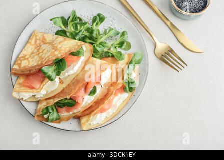 Crêpes ou crêpes fines avec saumon légèrement salé, fromage à pâte molle et salade de maïs ou laitue d'agneau sur une assiette vue de dessus de gros plan sur backgro texturé clair Banque D'Images