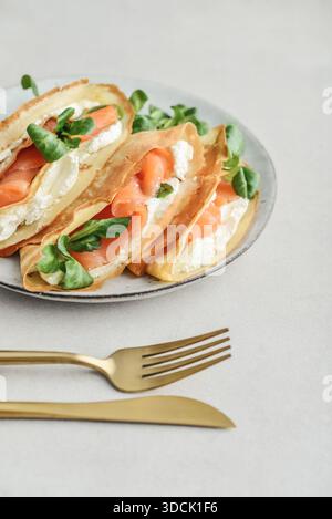 Crêpes ou crêpes fines avec saumon légèrement salé, fromage à pâte molle et salade de maïs ou laitue d'agneau sur une assiette vue de dessus de gros plan sur backgro texturé clair Banque D'Images
