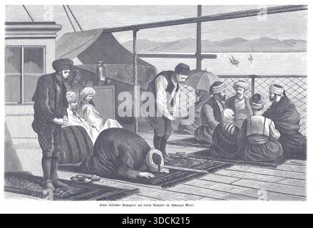 Un groupe d’hommes musulmans effectue la prière commune sur le pont d’un navire, s’agenouillant et s’inclinant sur des tapis de prière tandis que d’autres s’assoient à proximité, créant un moment de réveillon Banque D'Images