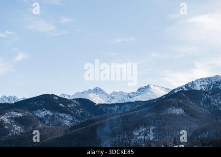 Les pics spectaculaires et ensoleillés des montagnes Tatra (y compris la croix de Giewont) s'élèvent au-dessus de sombres contreforts boisés sous un ciel bleu vif. W Banque D'Images