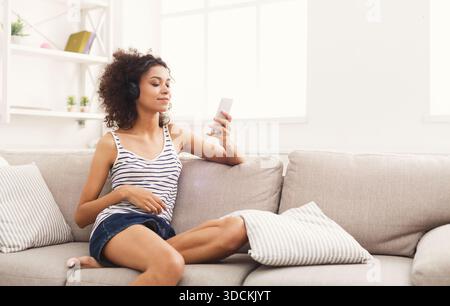 Heureuse jeune femme dans des écouteurs sur un canapé beige Banque D'Images
